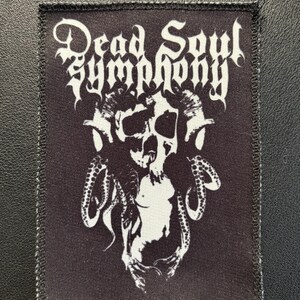 Può includere: Una toppa rettangolare in tessuto nero con bordo ricamato bianco. Il design presenta la scritta bianca Dead Soul Symphony sopra un grafico di un teschio con corna e tentacoli che si estendono verso il basso su entrambi i lati.