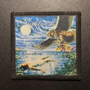 Könnte beinhalten: Ein quadratischer Stoffaufnäher mit schwarzem Rand und einem Nightwish Oceanborn-Motiv. Das Bild zeigt eine Eule, die über einem mondbeschienenen Gewässer fliegt und eine Schriftrolle in ihren Krallen hält, während eine Figur im Wasser schwimmt.