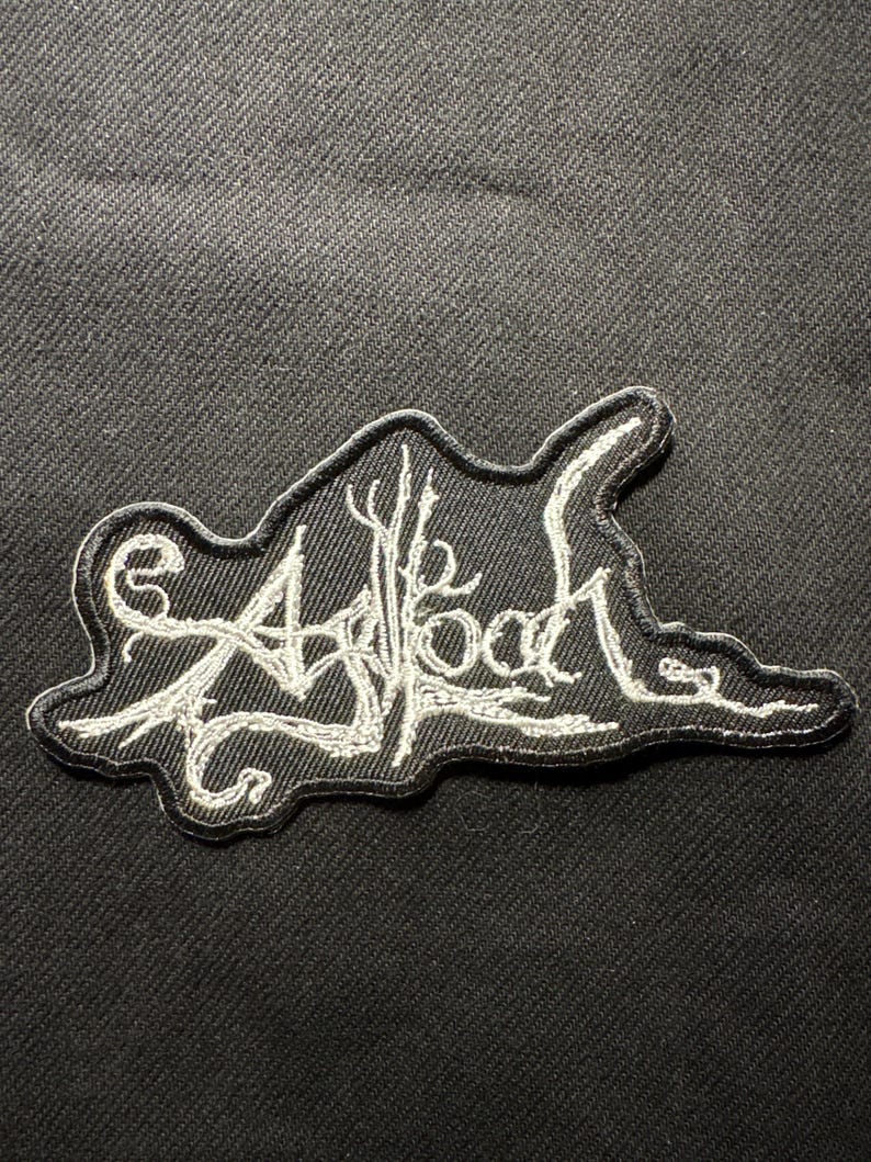 Puede incluir: Parche bordado negro con costuras blancas. El parche presenta la palabra "Asblood" en una fuente estilizada, con un dise&ntilde;o en forma de &aacute;rbol incorporado en las letras. El parche est&aacute; sobre un fondo de tela negra.