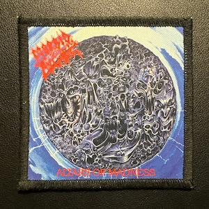 Puede incluir: Parche cuadrado con borde negro. Presenta una ilustración oscura y detallada dentro de un diseño circular azul y blanco. El parche incluye el texto "ALTAR OF MADNESS" en rojo.