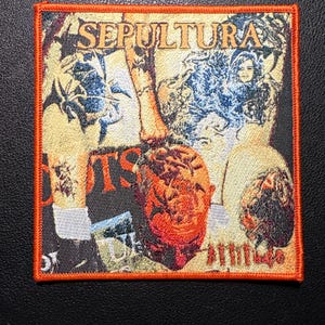 Könnte beinhalten: Quadratischer Aufnäher mit orangefarbenem Rand und dem Bandnamen "SEPULTURA" in goldfarbenen Buchstaben. Der Aufnäher hat ein Collage-Design mit Bildern in Orange-, Blau- und Schwarztönen. Das Wort "ROOTS" ist ebenfalls sichtbar.