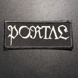 Op de afbeelding: Een rechthoekige zwarte patch met het woord "PORTAL" in witte, gotische letters geborduurd. De patch heeft een zwarte rand en is waarschijnlijk bedoeld om op kleding of accessoires te worden genaaid.