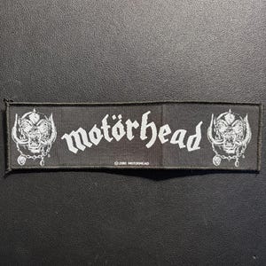 May include: Black rectangular patch featuring the band name "motörhead" in white, stylized lettering. The patch includes a skull logo on each side and the text "© 2010 MOTÖRHEAD" at the bottom. The patch is likely for clothing or accessories.