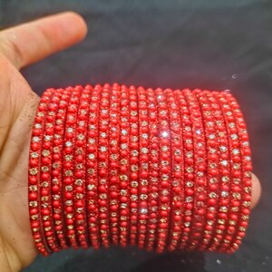 Pode incluir: Uma pilha de pulseiras vermelhas, cada uma adornada com pequenos enfeites brilhantes. As pulseiras são de uma cor vermelha vibrante e parecem ser feitas de um material de contas. A estética geral é a de uma joia festiva.