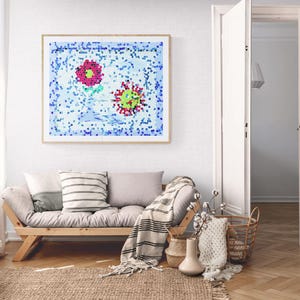 Może przedstawiać: Salon z oprawionym dziełem sztuki przedstawiającym dwa abstrakcyjne kwiaty w kolorze różowym i zielonym. Jasna drewniana sofa futon z poduszkami i kocem stoi na tkanej macie. Dekoracyjne kosze i wazony dopełniają wystroju pokoju.