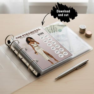 A printable $180 financial savings challenge tracker for an A6 binder, shown inside a clear six-ring binder with a pen and coins on the wooden table, illustrating the 'Download and cut' instruction.