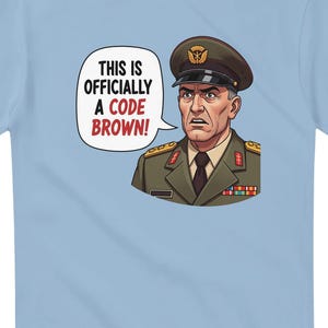 Op de afbeelding: Lichtblauw T-shirt met een cartoon illustratie van een streng kijkende militaire officier in een bruin uniform en hoed. Een tekstballon zegt: "THIS IS OFFICIALLY A CODE BROWN!"
