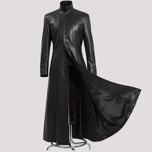 May include: A long, black leather coat with a mandarin collar and button-up front. The coat is floor-length and has a flowing design, with one side open to reveal the lining. The coat is displayed on a metal mannequin.