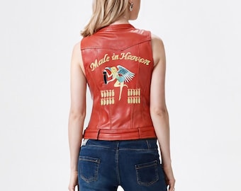 May include: A red leather vest with the text "Male in Heaven" embroidered on the back. The vest features a colorful embroidered design of a figure with wings and other decorative elements. The vest has a classic biker style with a belt.