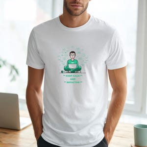 Könnte beinhalten: Weißes T-Shirt mit einer Cartoon-Illustration einer Person, die mit gekreuzten Beinen und einem Laptop sitzt. Die Person trägt eine Brille und grüne Kleidung. Der Text "KEEP CALM AND REFACTOR" ist darunter gedruckt.