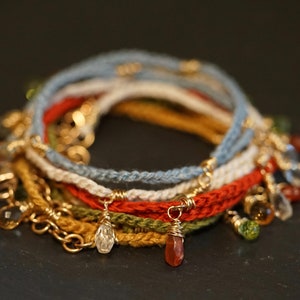 Puede incluir: Un conjunto de seis pulseras de crochet con detalles dorados y abalorios de piedras preciosas. Las pulseras son en tonos de azul, blanco, rojo, verde y amarillo.