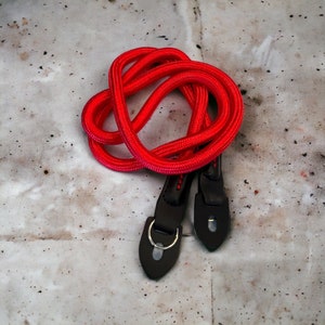 May include: A red camera strap with black leather ends and metal rings.