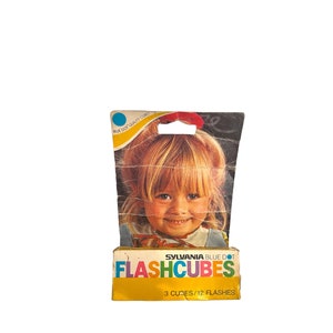 May include: A yellow and blue package of Sylvania Blue Dot Flashcubes. The package features a smiling child and the text "FLASHCUBES 3 CUBES/12 FLASHES".