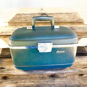 May include: A vintage green travel case with a silver lock and handle. The case has a silver trim and the word "Shwayder" is printed on the front.