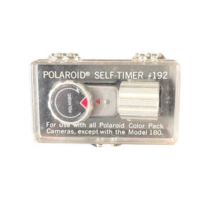 May include: A Polaroid Self-Timer #192 in a clear plastic case. The timer has a silver dial with a red arrow and the text "POLAROID" printed on it. The text "For use with all Polaroid Color Pack Cameras, except with the Model 180." is printed on the case.