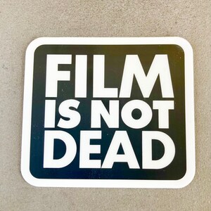 May include: A white sticker with a black border and the text "FILM IS NOT DEAD" in white letters.