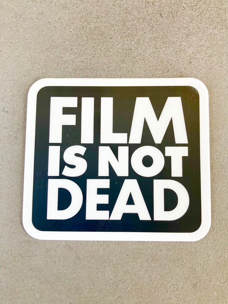 May include: A white sticker with a black border and the text "FILM IS NOT DEAD" in white letters.