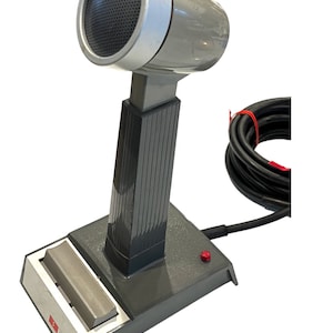 May include: A gray desktop microphone with a black cord and a red button on the base. The microphone has a silver top and a black grill.