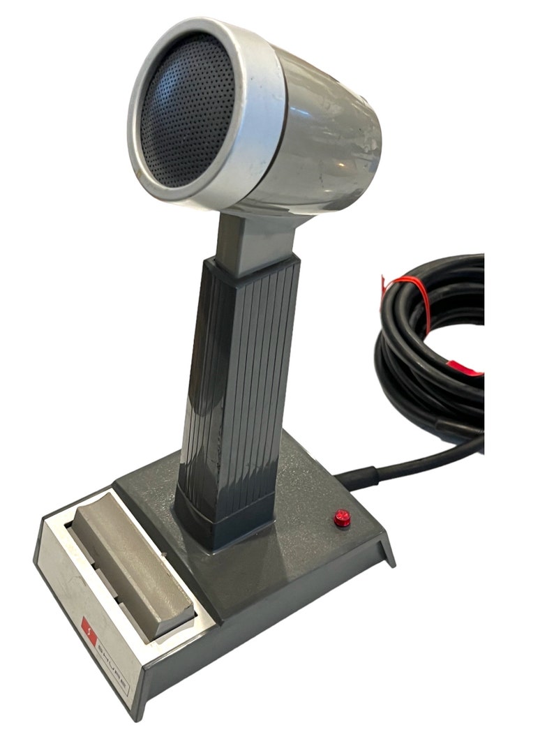May include: A gray desktop microphone with a black cord and a red button on the base. The microphone has a silver top and a black grill.