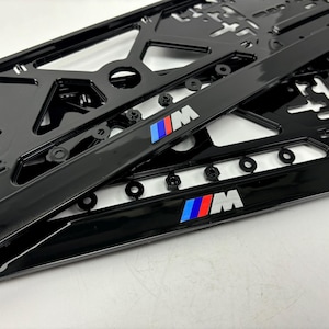 Può includere: Due cornici nere per targa con il logo "M" in blu, rosso e bianco. Le cornici hanno una finitura lucida e sono progettate con più fori e fessure per il montaggio. Le cornici sono per un veicolo.