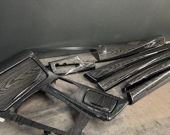 May include: A collection of automotive interior trim pieces with a dark wood grain finish. The set includes various dashboard and console components, showcasing a modern, textured aesthetic. The pieces are arranged on a neutral surface.