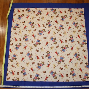 May include: A rectangular quilt with a cream-colored patterned center and a blue border. The pattern features cowboys, dogs, and red polka dots. A yellow and white measuring tape is visible.