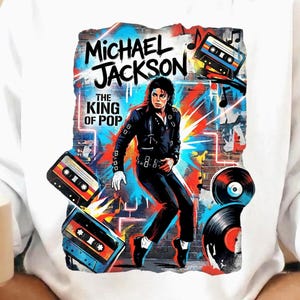 May include: White sweatshirt with a graphic of Michael Jackson, the text reads "MICHAEL JACKSON THE KING OF POP." The design incorporates cassette tapes and vinyl records. The image is a colourful, graffiti-style design.