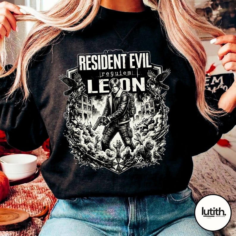 Może przedstawiać: Czarna bluza z grafiką z gry "Resident Evil: Requiem". Projekt zawiera tekst "Resident Evil" i "Leon", a także ilustrację postaci z bronią, otoczonej przez zombie i kruki.
