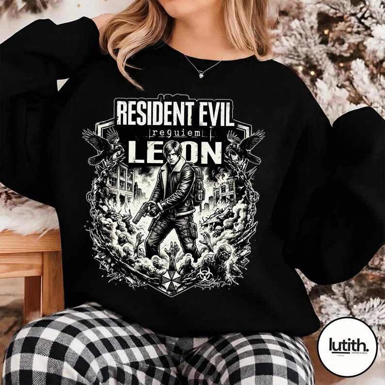 Może przedstawiać: Czarna bluza z grafiką z Resident Evil. Projekt zawiera tekst "Resident Evil | requiem | Leon" oraz ilustrację postaci trzymającej broń, otoczonej przez zombie i budynki.