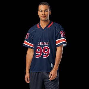 May include: Navy blue jersey with red and white accents. The jersey features the word "LIBAS" above the number "99" in white with a red outline. The sleeves have white stripes with red trim. A small logo is on the lower right.