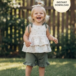 K&ouml;nnte beinhalten: Ein l&auml;chelndes Kleinkind tr&auml;gt ein zweistufiges Oberteil mit floralem Muster und olivgr&uuml;ne Shorts. Das Oberteil hat olivgr&uuml;ne Tr&auml;ger und die Shorts einen R&uuml;schensaum. Das Kind tr&auml;gt wei&szlig;e Schuhe und ein passendes Stirnband. Der Text "INSTANT DOWNLOAD" ist sichtbar.