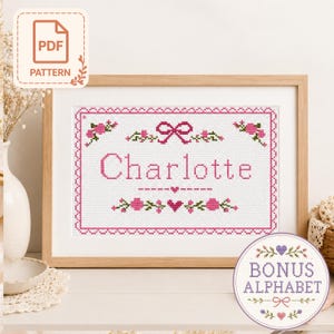 May include: A cross stitch pattern featuring the name Charlotte in pink letters, surrounded by a pink floral border, a bow, and hearts. The design includes a PDF pattern label and a circular bonus alphabet graphic with floral accents.