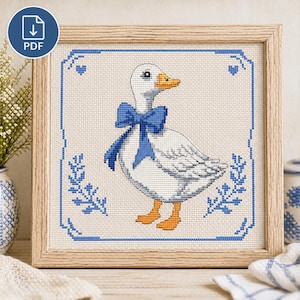 May include: Cross-stitch pattern of a white goose wearing a blue bow, framed in a wooden square. The design features blue floral and heart accents. The PDF download icon is in the upper left corner.