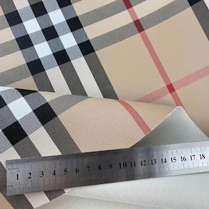 May include: Close-up of a beige fabric with a classic plaid pattern in black, white, and red. A metal ruler with millimeter markings is placed on the fabric. The ruler measures up to 18 cm.