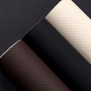 Peut inclure: Gros plan sur des échantillons de cuir perforé de différentes couleurs. Les échantillons comprennent du noir, du blanc cassé et du marron. Le cuir présente un motif uniforme de petits trous espacés, créant un aspect texturé. Les bords du cuir sont visibles.
