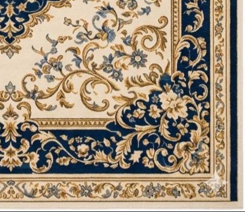 May include: A rectangular area rug featuring a cream-colored background with a deep blue border. The design includes intricate gold and blue floral patterns, scrolling vines, and acanthus leaf motifs that create a symmetrical, ornate composition.