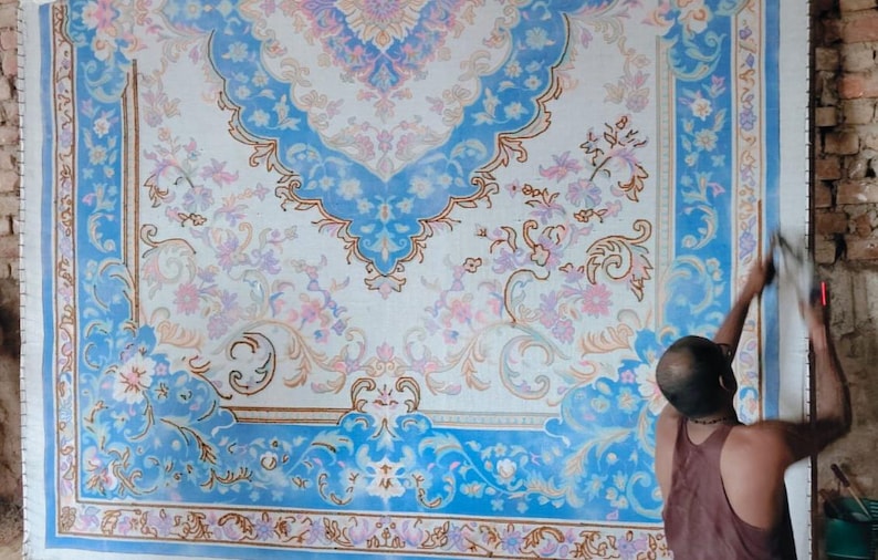 May include: A large rectangular rug featuring a white background with intricate blue and light pink floral patterns. The design includes a central medallion and ornate borders with scrolling vines and blossoms, creating a symmetrical layout.