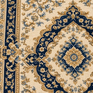 May include: A woven area rug featuring a cream-colored background with intricate floral and medallion patterns in deep blue and golden tan. The design includes a wide border with repeating floral motifs and a central diamond-shaped medallion.