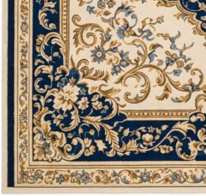 May include: A rectangular area rug featuring a cream-colored center with intricate blue and gold floral scrollwork. The border consists of a deep blue frame adorned with gold leaf patterns and a thin outer cream edge with small floral motifs.