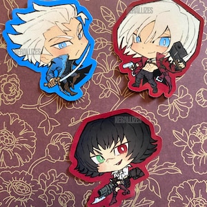 May include: Three die-cut stickers featuring chibi-style anime characters. One character has white hair and a blue coat with a sword, another has white hair and a red coat with two handguns, and the third has black hair and holds a large firearm.