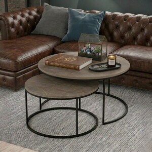 Peut inclure: Ensemble de deux tables basses rondes avec un plateau aspect marbre gris foncé et des cadres en métal noir. Les tables sont gigognes, avec une petite table en dessous. Un livre, une bougie et des objets décoratifs sont sur la table supérieure.