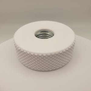 Peut inclure: Un objet cylindrique blanc avec un côté texturé en losanges et un trou fileté central. Le dessus est plat et lisse, tandis que le trou révèle un filetage métallique. Il s'agit probablement d'un composant ou d'une fixation.