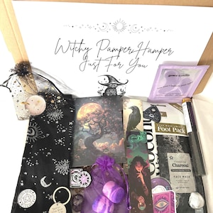 May include: A Witchy Pamper Hamper gift box containing self-care items. Includes a black sock with moon and star designs, a bookmark, face mask, bath bombs, and other mystical accessories. The box lid reads "Witchy Pamper Hamper Just For You."