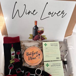 May include: A wine-themed gift box containing black socks with wine glass patterns, a wooden coaster with the text "But first Wine", and a bottle stopper. Also includes a keychain and two prescription-style cards.