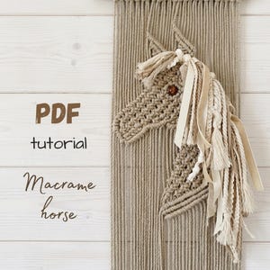 Könnte beinhalten: Ein Makramee-Pferd als Wandbehang aus beigefarbenem Garn mit einem braunen Perlenauge und einer Mähne aus gemischten Bändern und Garnen. Der Text links lautet PDF tutorial Macrame horse. Das Design zeigt einen Hintergrund aus vertikalen Kordeln.