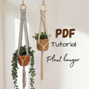 May include: Two macrame plant hangers with wooden rings, one in light gray and one in cream, each holding a potted plant. The text PDF Tutorial Plant hanger is displayed on the right side of the image in brown and black lettering.