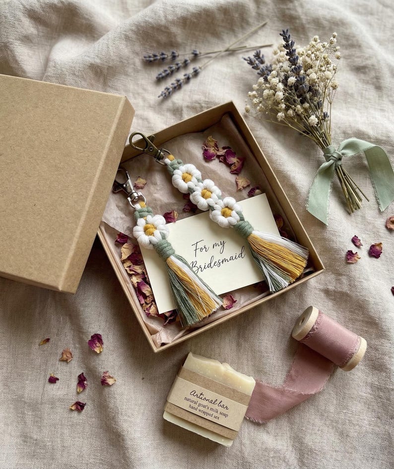 Handcrafted daisy macrame keychain gift for bridesmaid in a rustic box with proposal card, styled with dried petals, lavender and natural craft elements.