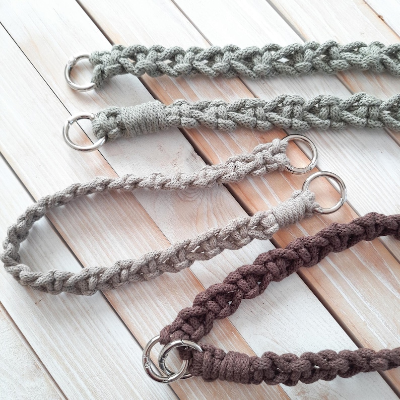 Peut inclure: Quatre anses de sac en macram&eacute; dans les tons de gris et de marron, chacune avec un anneau en m&eacute;tal argent&eacute;. Les anses sont faites de cordon de coton tiss&eacute; et sont pr&eacute;sent&eacute;es sur une surface en bois clair.