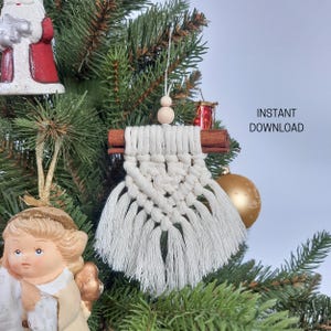 May include: A handmade macrame Christmas ornament with a cinnamon stick accent. The white cotton fiber is knotted into a decorative design with a fringed bottom. The text "INSTANT DOWNLOAD" is visible in the background.