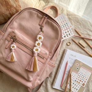 Handcrafted daisy macrame keychain clipped to a backpack, boho zipper charm made from cotton cord with floral pattern and tassel.